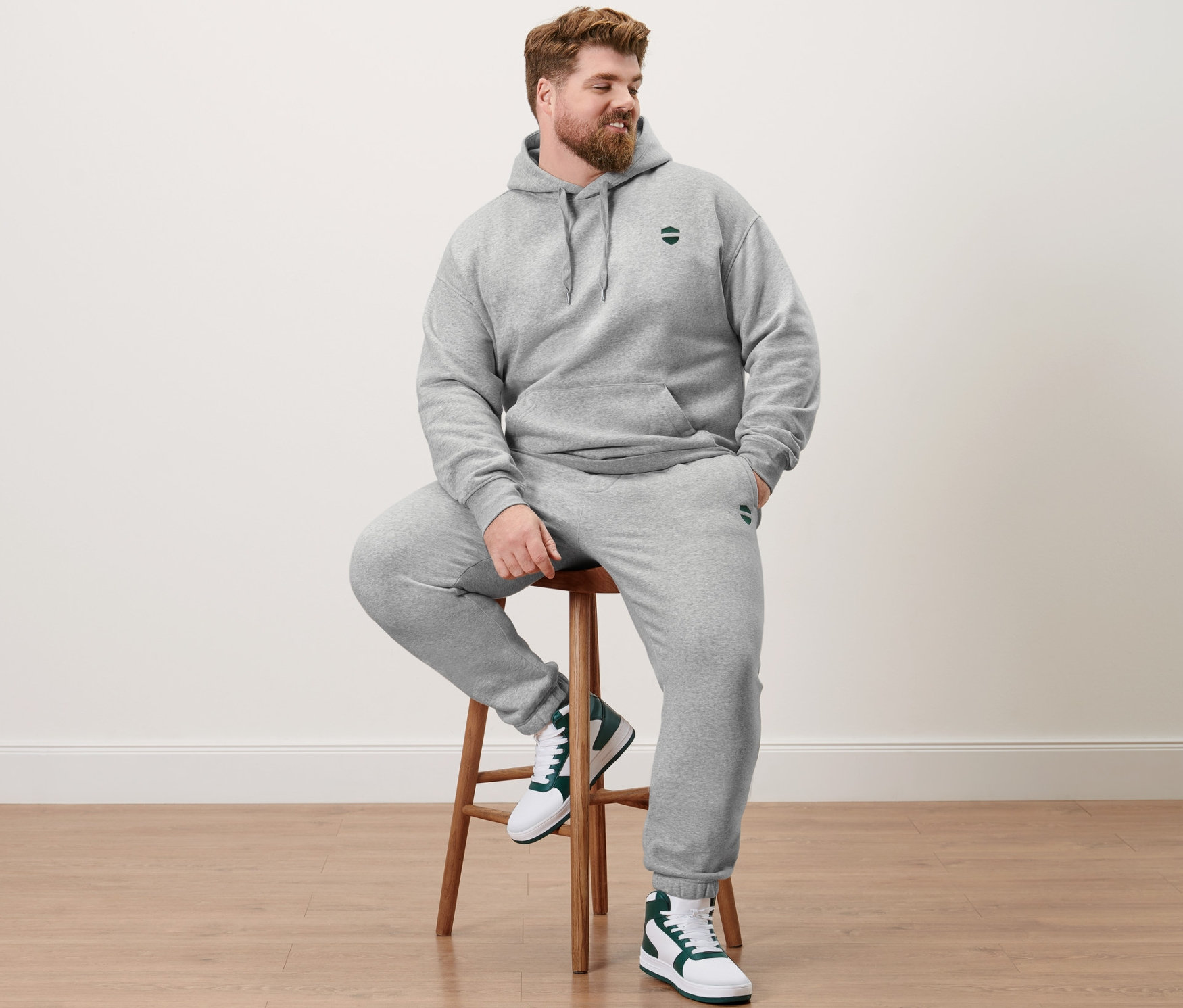 Mann sitzt auf einem Hocker und trägt einen graumelierten Hoodie und eine Sweathose.