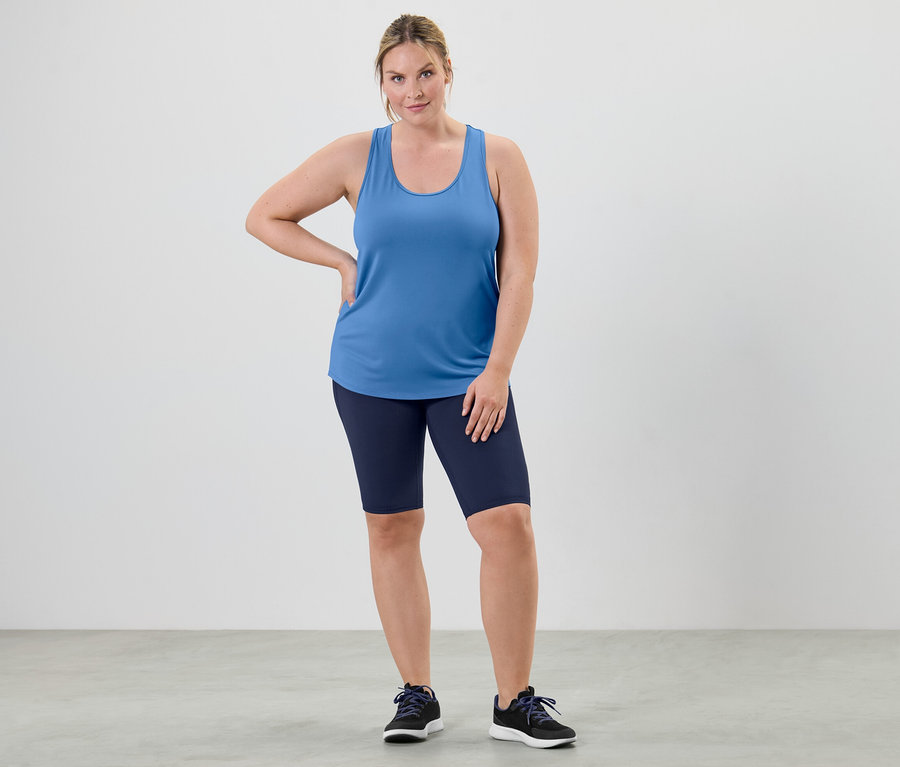 Eine Frau posiert in einem himmelblauen Funktionsstop aus einem zweiteiligen Set und Radlershorts.