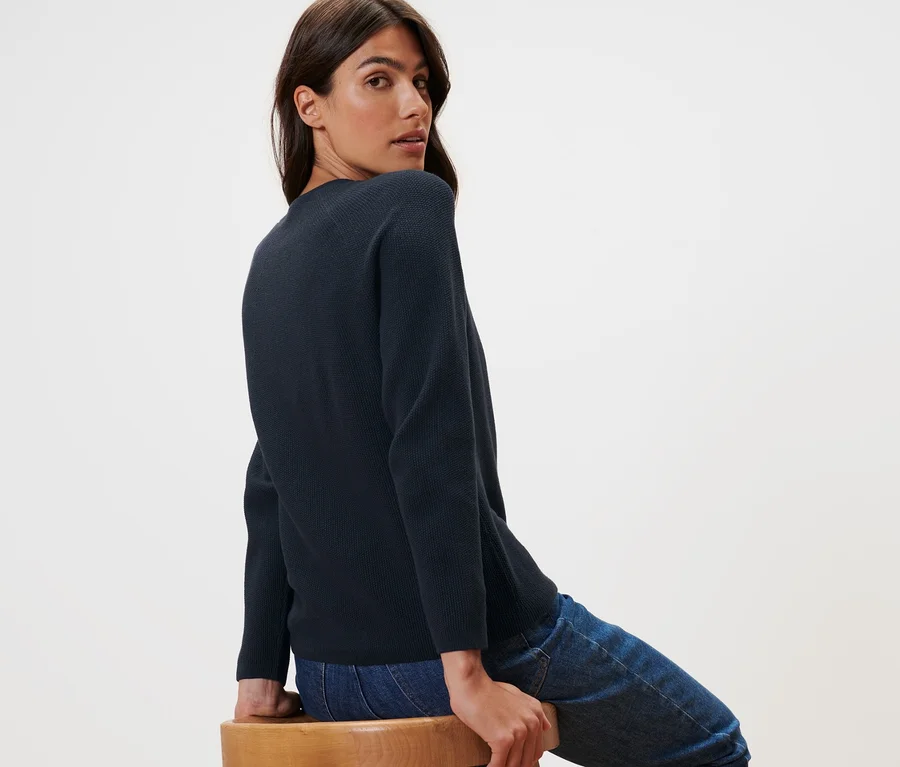 Frau sitzt auf einem Holzstuhl und trägt einen dunkelblauen Strickpullover.