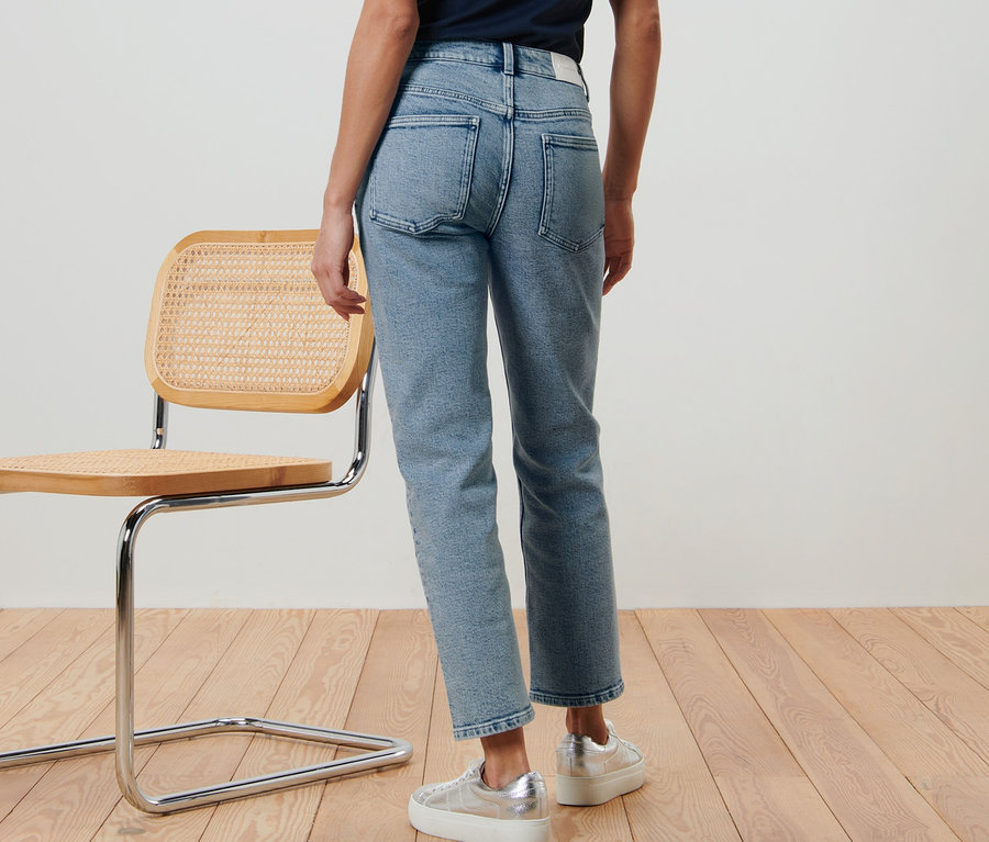 Eine Frau steht mit dem Rücken zur Kamera und trägt eine moderne Jeans – Fit »Ava« und silberne Turnschuhe.