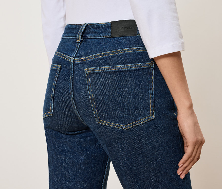 Rückansicht einer Frau in hochgeschnittenen, blauen Jeans und einem weißen T-Shirt.