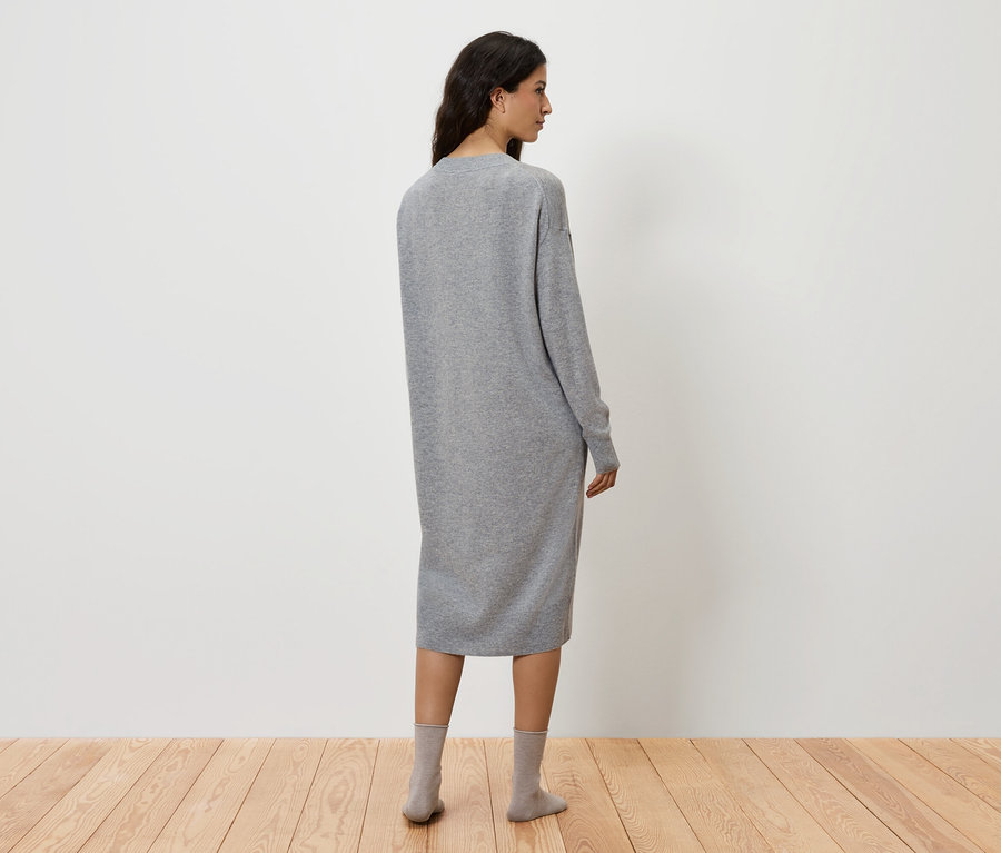Frau steht mit dem Rücken zur Kamera und trägt ein graues Kleid und graue Socken.