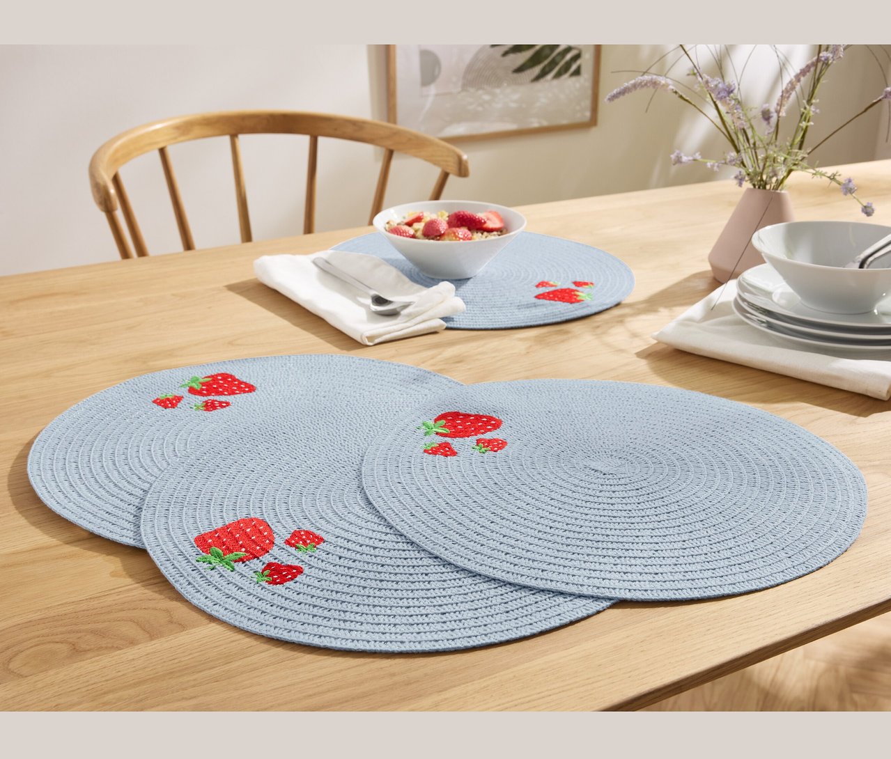 Vier blaue Platzsets mit Erdbeeren auf einem Holztisch.