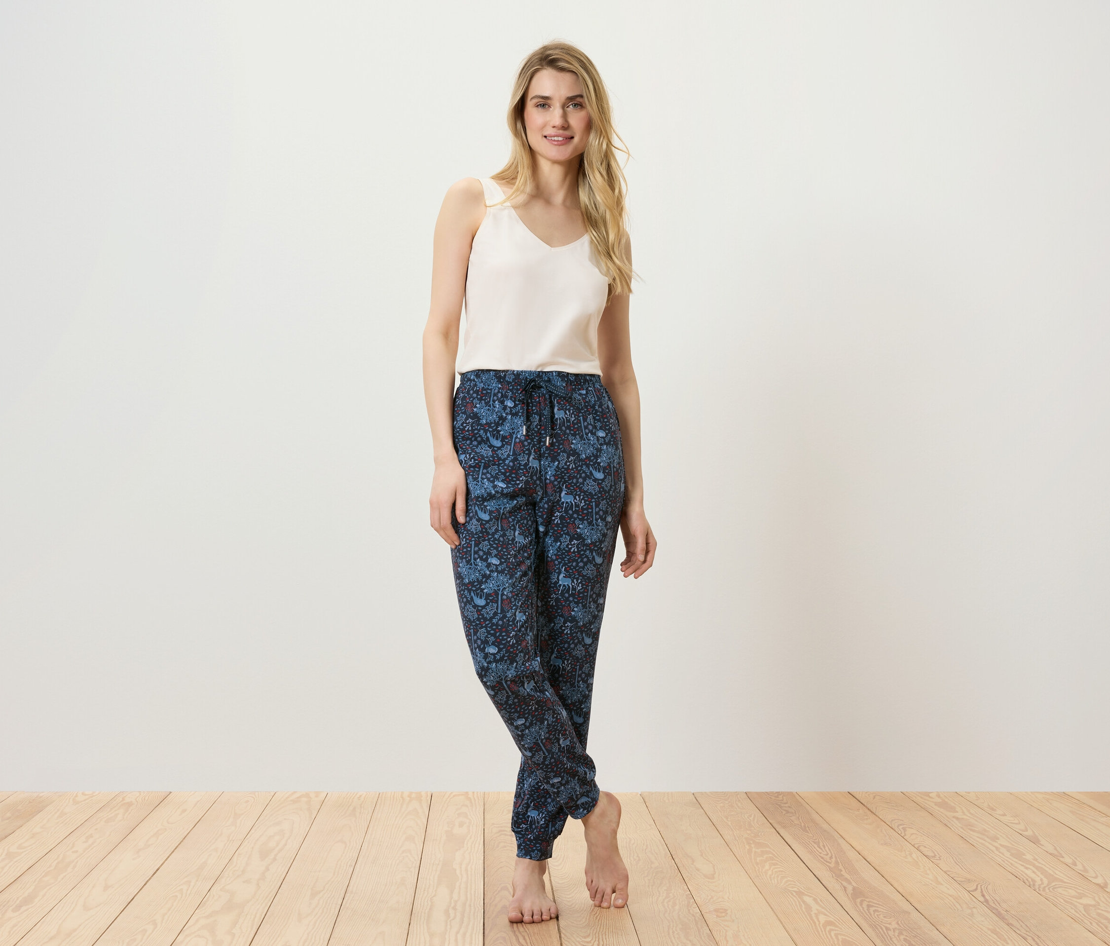 Frau posiert in Tanktop und gemusterter Hose auf Holzboden.