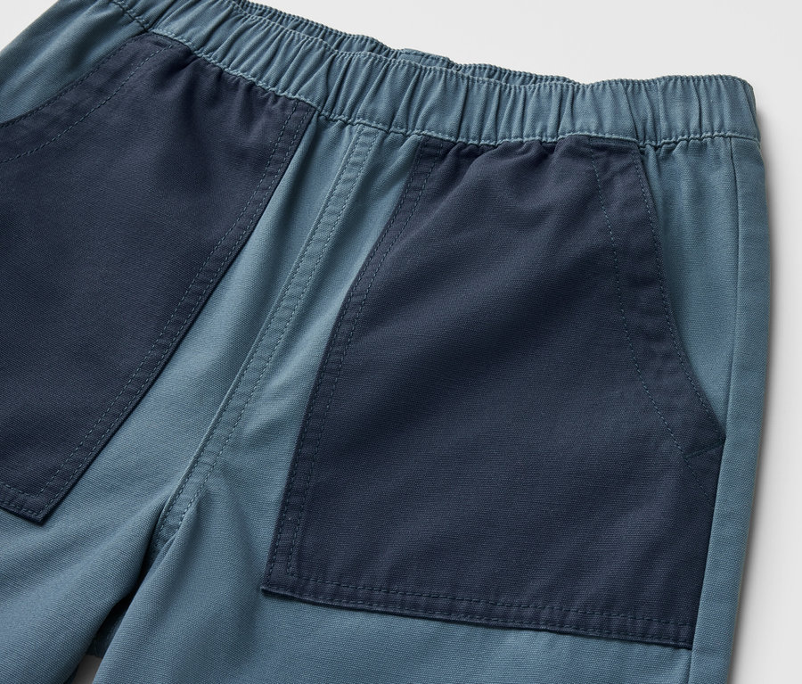 Detailaufnahme von Kinder-Bermudashorts mit dunkelblauen Taschen auf hellblauem Grund.