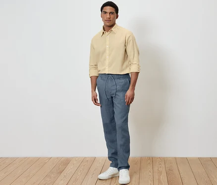 Mann steht und trägt eine blaue Leinen-Chino und ein gelbes Hemd.