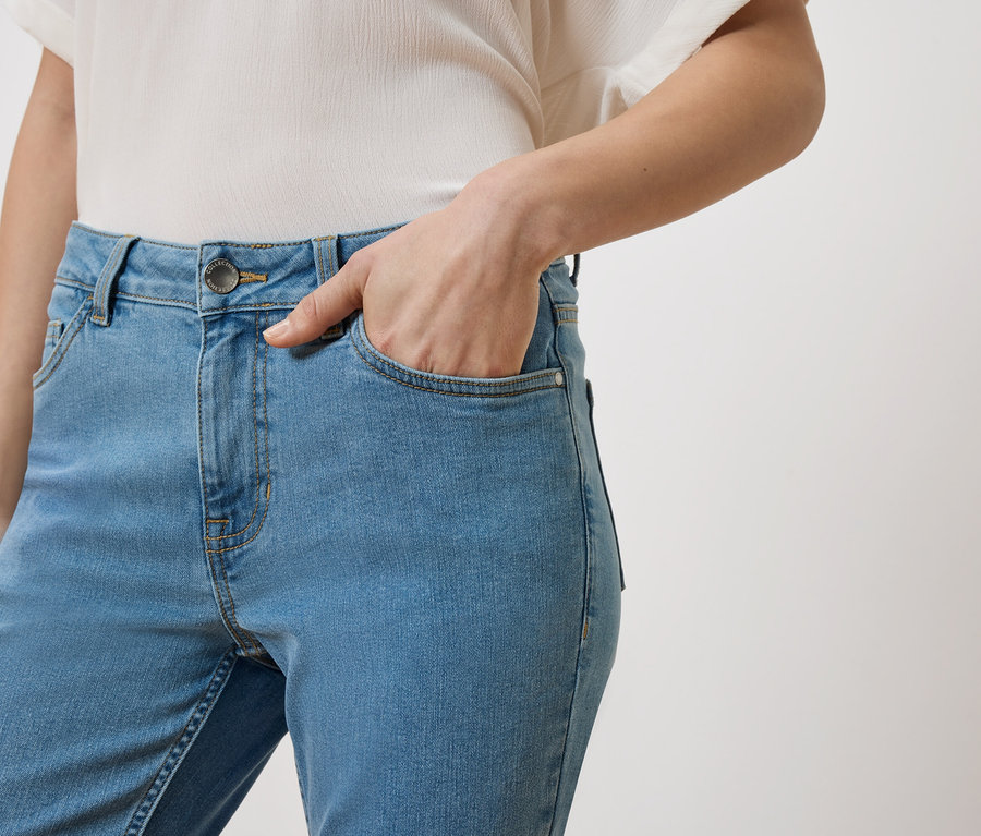 Frau mit Hand in der Tasche einer hellblauen Jeans, dazu ein weißes Oberteil.