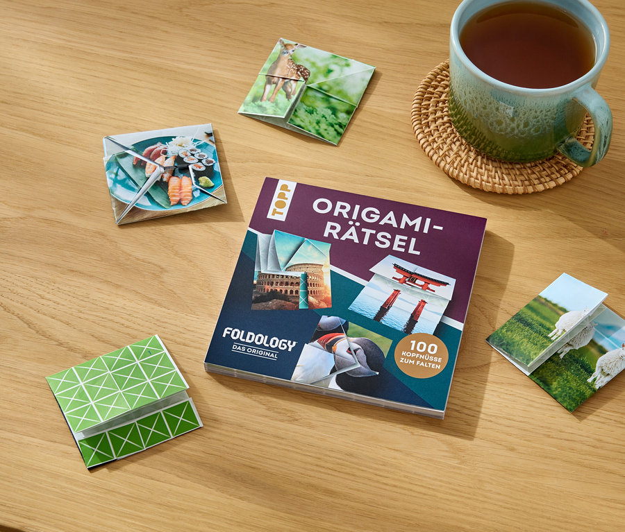 Auf einem Holztisch liegen das Buch »Origami-Rätsel«, eine Tasse Tee und gefaltete Origami-Figuren mit verschiedenen Motiven.
