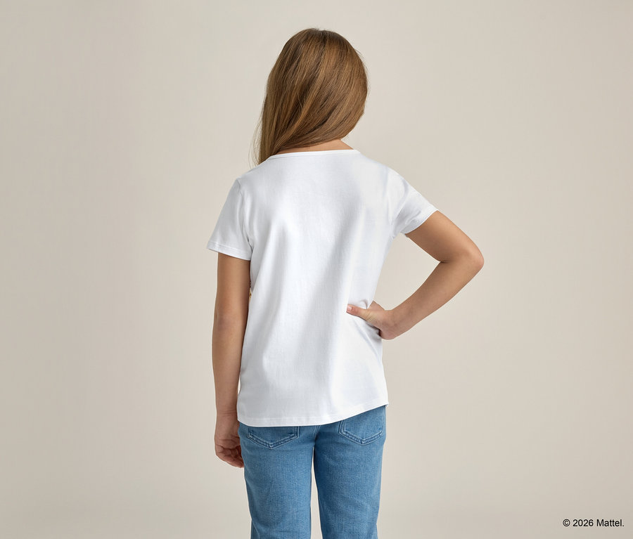 Mädchen mit blonden Haaren, von hinten gesehen, trägt ein weißes T-Shirt und blaue Jeans, die Hand in der Hüfte.