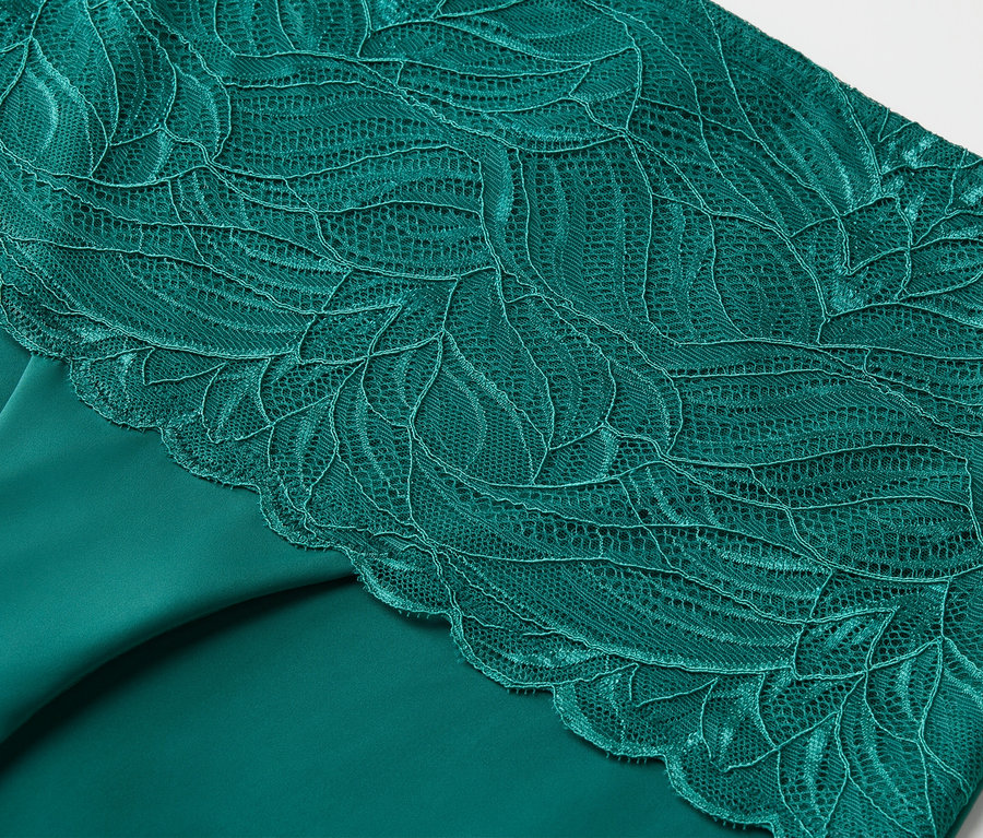Detailaufnahme eines smaragdgrünen Stoffes mit floraler Spitze.