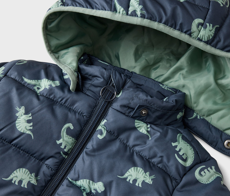 Nahaufnahme einer marineblauen, gesteppten Jacke mit Kapuze und Dinosaurier-Muster. Die Innenseite der Kapuze ist hellgrün.