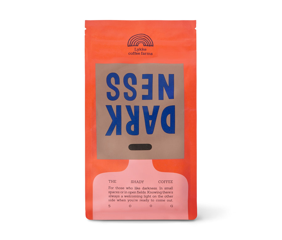 Orangefarbene Kaffeepackung von Lykke coffee farms mit einem braunen Etikett, auf dem "DARK NESS" in blauen, spiegelverkehrten Buchstaben steht. Die Packung enthält 500 g Lykke DARKNESS Omni-Roast Ganze Bohne.
