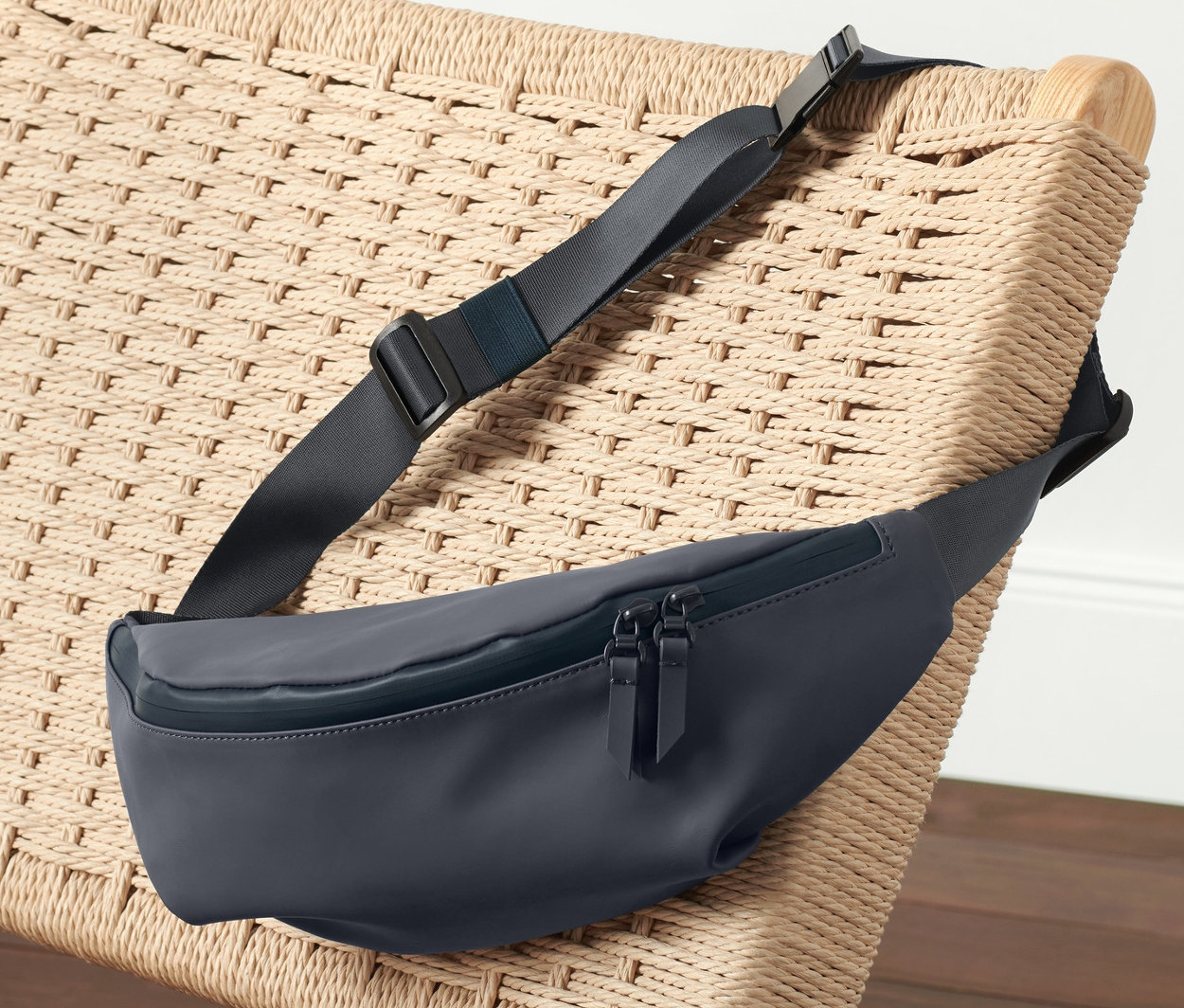 Eine marineblaue Hüfttasche liegt auf einem Korbsessel neben rosa Sportbekleidung.