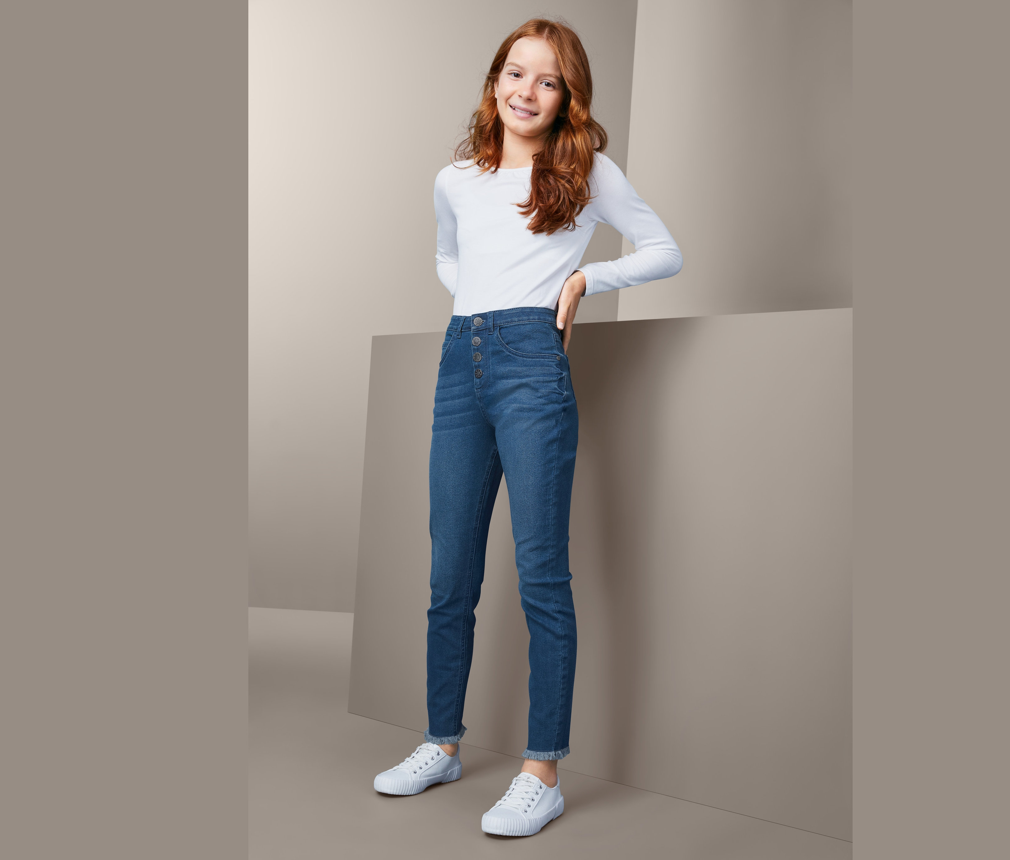Mädchen posiert in blauen High-Waist-Jeans und weißem Langarmshirt.