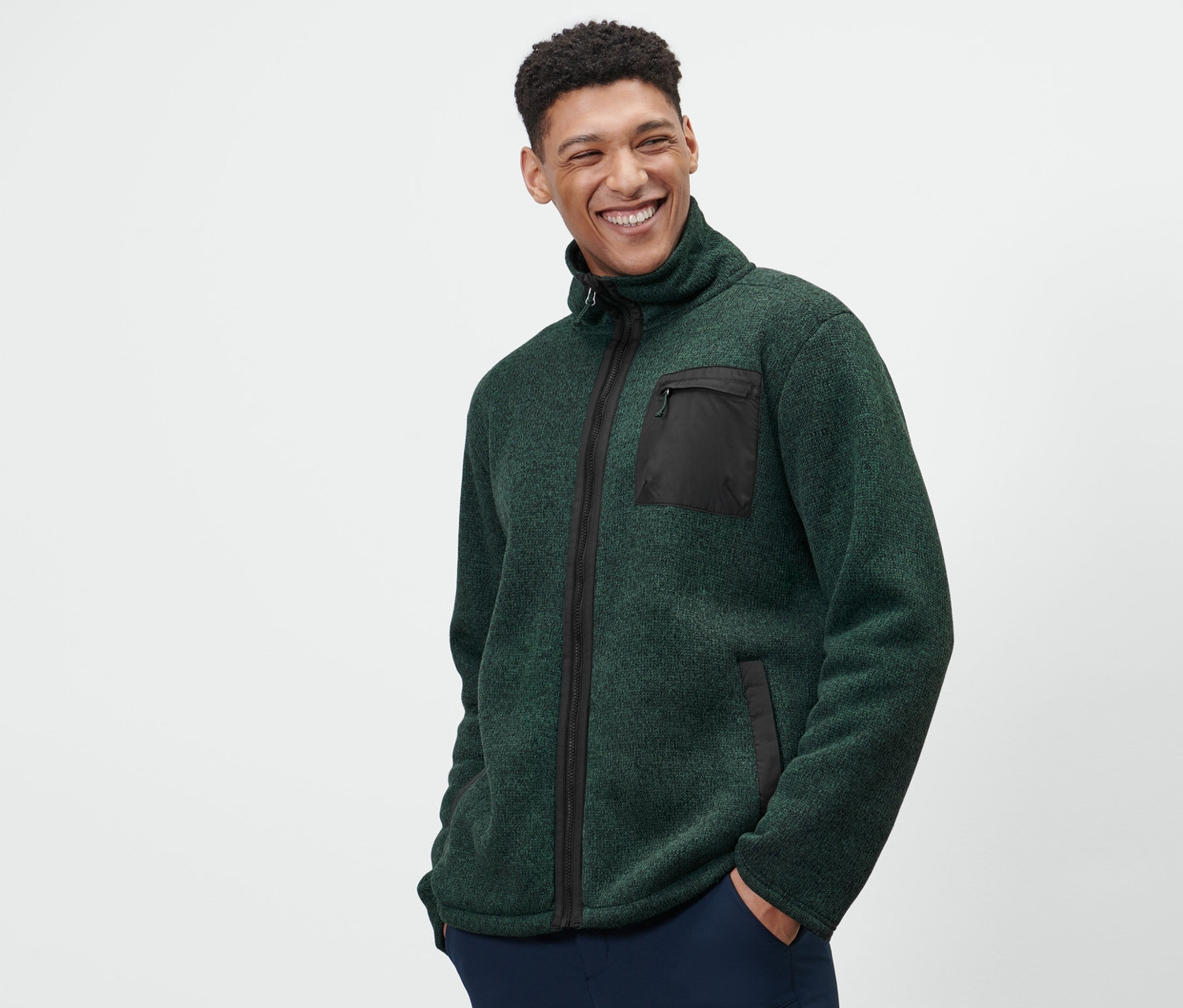 Ein Mann trägt eine grüne Thermo-Strickfleecejacke und dunkelblaue Hosen.