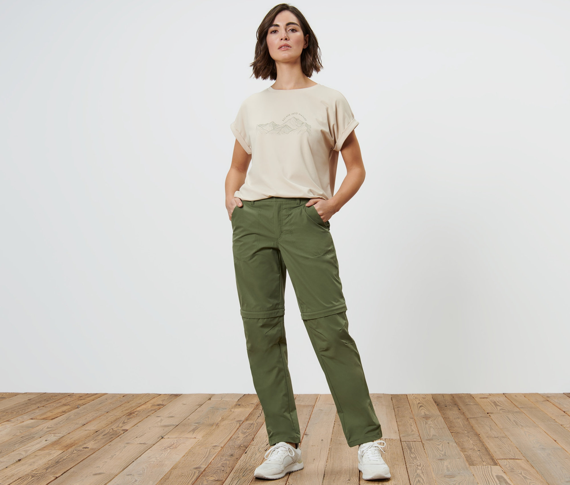 Eine Frau steht mit den Händen in den Taschen ihrer khaki-farbenen 2-in-1-Funktionshose.