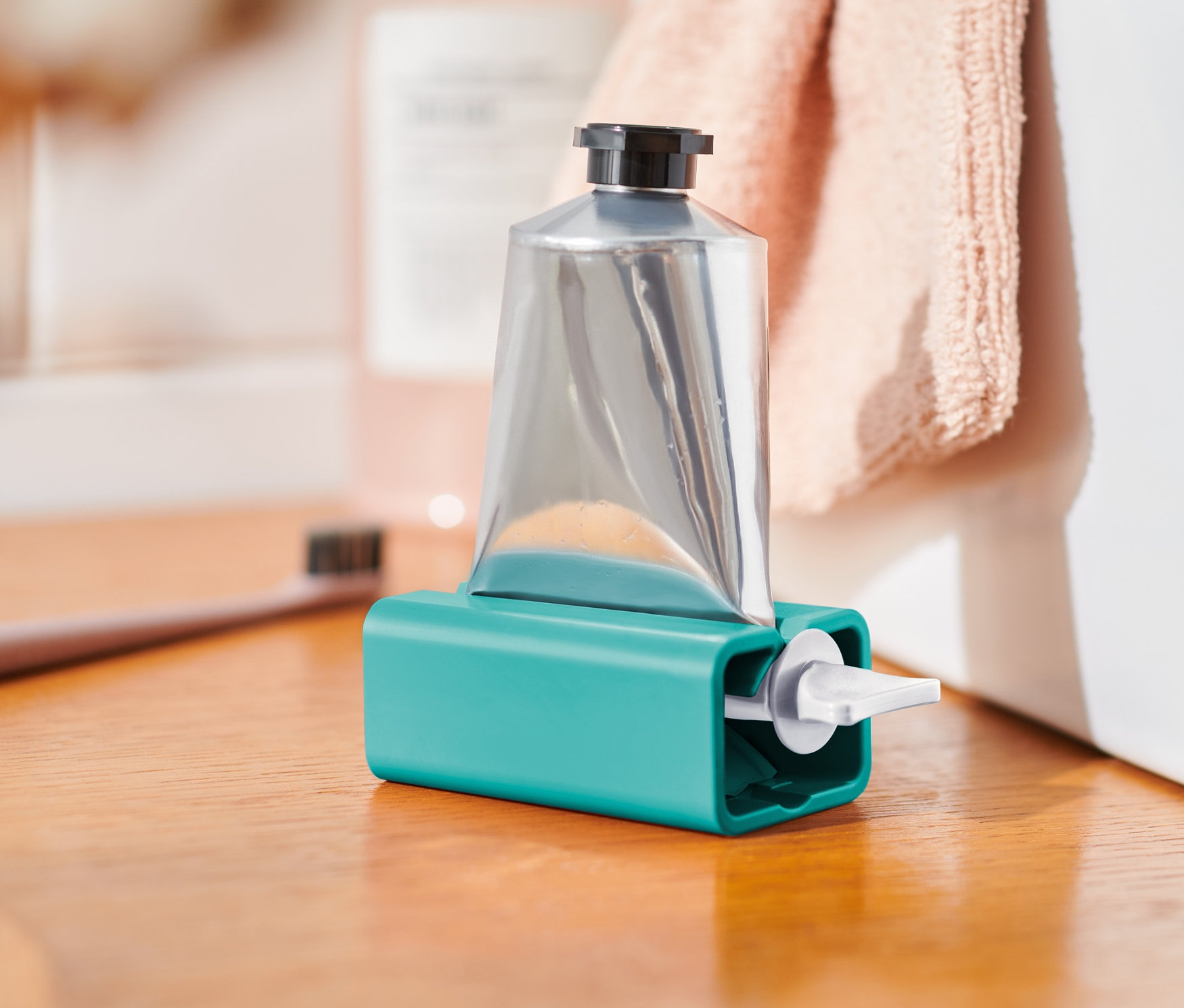 Silberne Tube in türkisfarbenem Tubenpresser auf einem Holzregal.