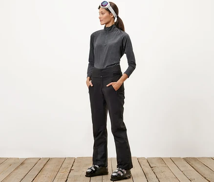 Frau steht mit Händen in den Taschen einer High-Waist-Skihose.