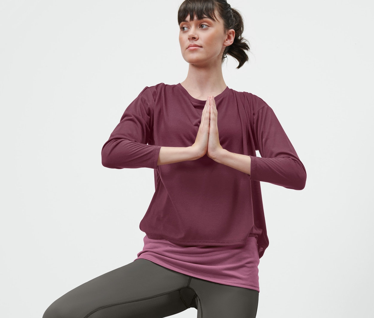 Frau in Baum-Pose auf einer Yogamatte, trägt ein 2-in-1-Sportshirt in Pflaume.