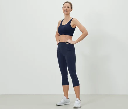 Frau posiert in dunkelblauem Sport-BH und 3/4 Sporttight.