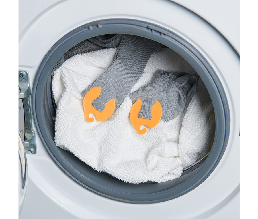 In einer Waschmaschine liegen ein Handtuch und zwei graue Sockenpaare, die mit 20 Socken-Clips verbunden sind.