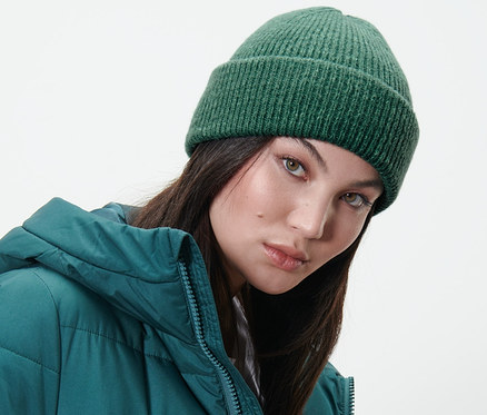 Frau trägt eine dunkelgrüne Strickmütze und eine grüne Daunenjacke.