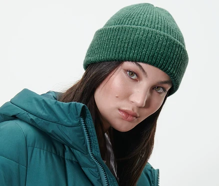 Frau trägt eine dunkelgrüne Strickmütze und eine grüne Daunenjacke.