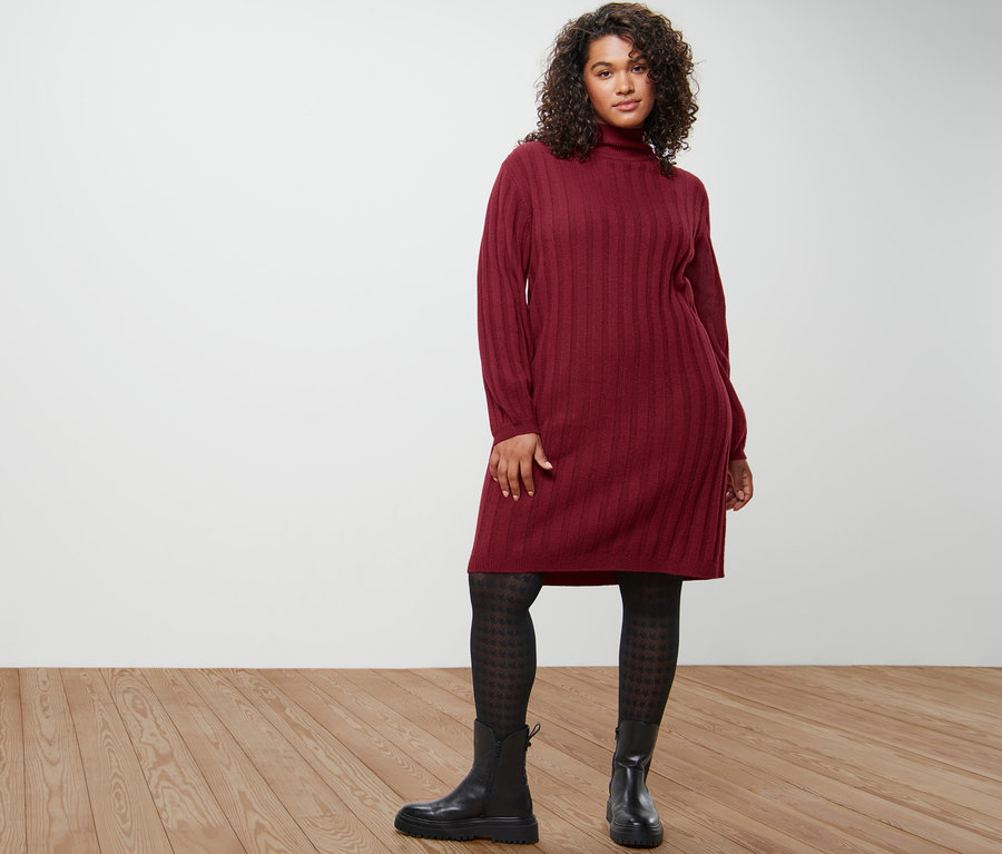 Frau posiert in geripptem Strickkleid mit Stehkragen, gemusterter Feinstrumpfhose und Leder-Boots.