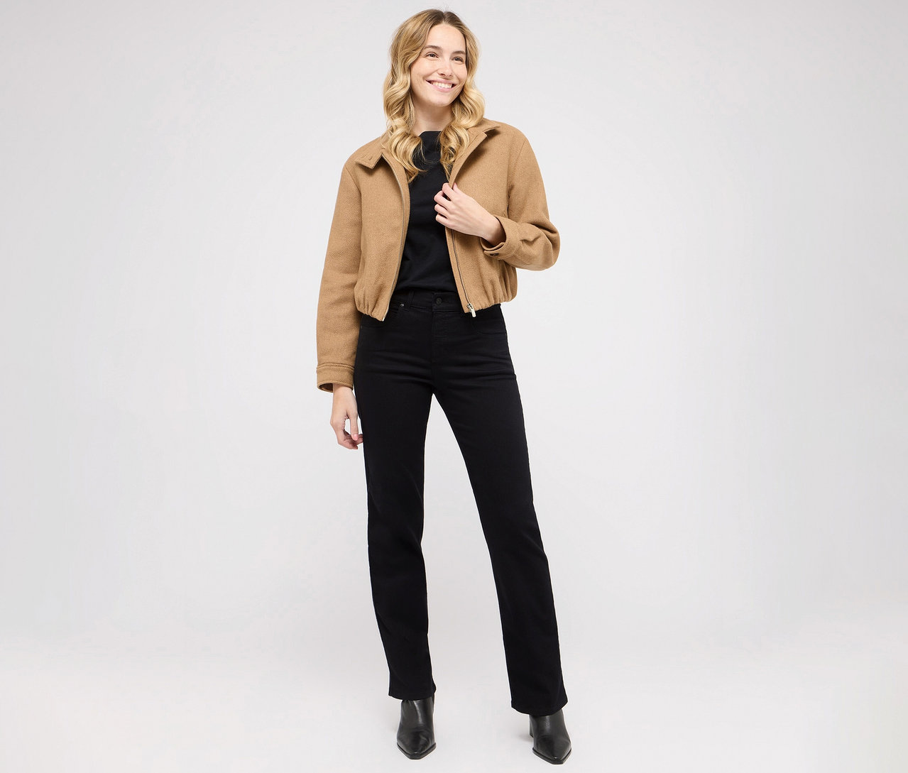 Frau posiert in Angels Denim »Lara« Straight Fit Jeans, schwarzem Oberteil und brauner Jacke.