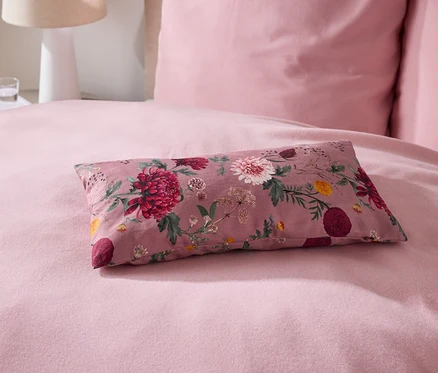 Auf einem Bett liegt ein rosafarbenes Kissen mit Blumenmuster.
