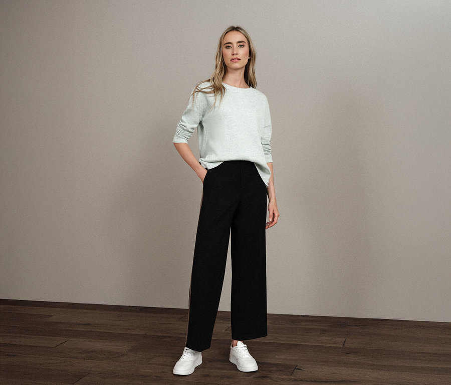 Frau steht mit der Hand in der Hosentasche und trägt ein Street One Shirt mit Struktur, eine schwarze Hose und weiße Turnschuhe.