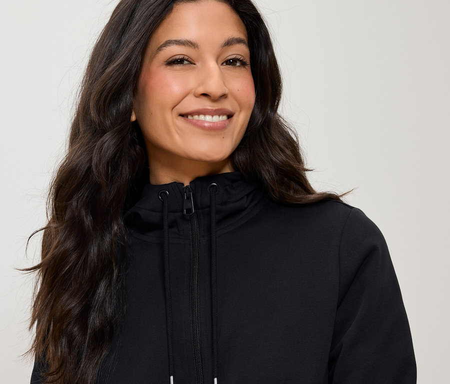 Porträt einer Frau mit langen braunen Haaren, die einen schwarzen Reißverschluss-Hoodie trägt.