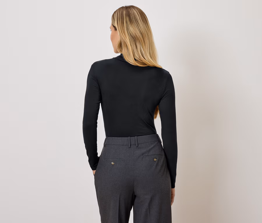 Rückansicht einer blonden Frau mit schwarzem Rollkragenpullover und grauer Hose.