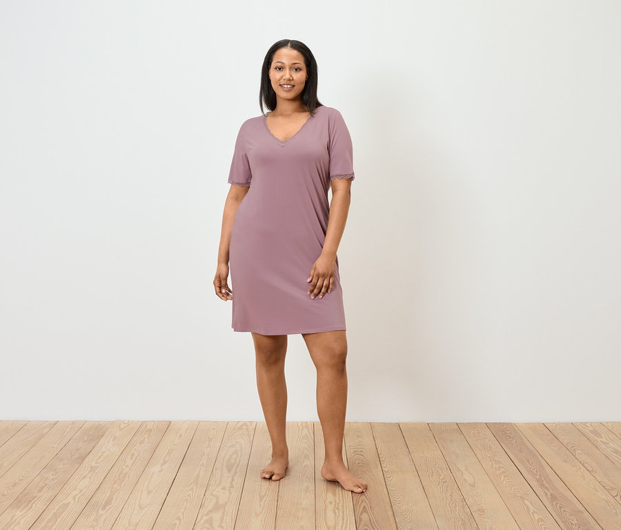 Frau steht barfuß und trägt ein kurzes, mauvefarbenes Nachthemd.