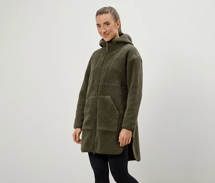 Frau trägt einen olivgrünen Kapuzenmantel und schwarze Leggings.