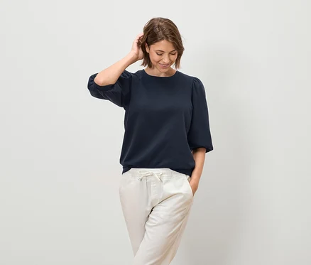Frau posiert in marineblauer Bluse mit kurzen Ärmeln und heller Hose.