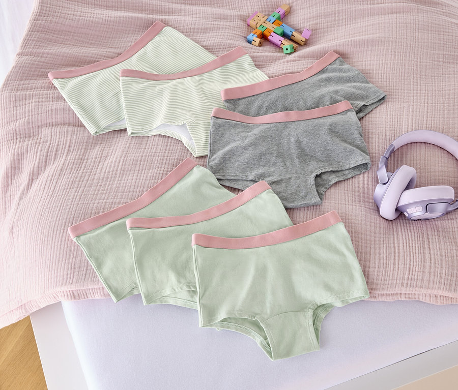 Auf einem Bett liegen sieben altrosa Mädchen-Pantys, ein Spielzeug und Kopfhörer.