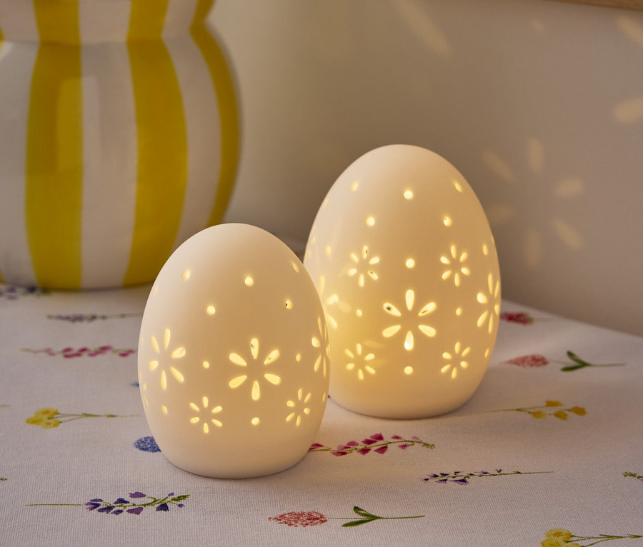 Zwei weiße, eiförmige Lampen mit Blumenmuster stehen auf einem Tisch mit einer Blumenvase im Hintergrund.