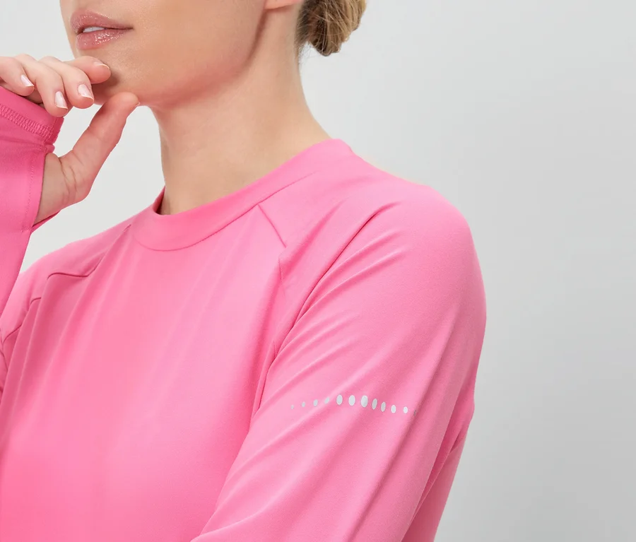 Frau in pinkem Langarmshirt mit Daumenlöchern, Hand am Kinn.