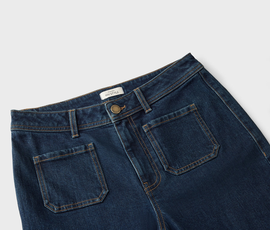 Nahaufnahme einer dunkelblauen Jeans mit aufgesetzten Taschen und hellbraunen Nähten.