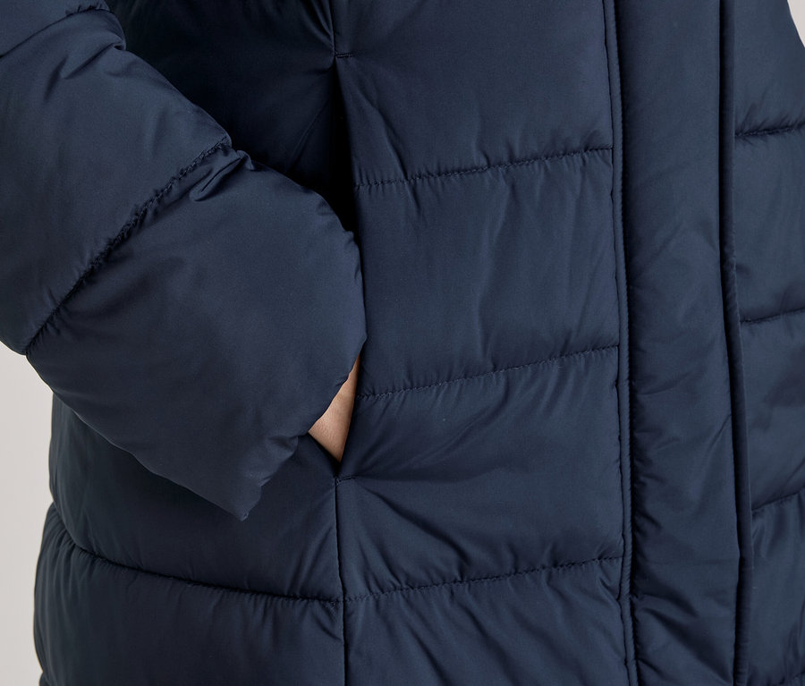 Hand steckt in der Seitentasche einer dunkelblauen, gesteppten Daunenjacke.
