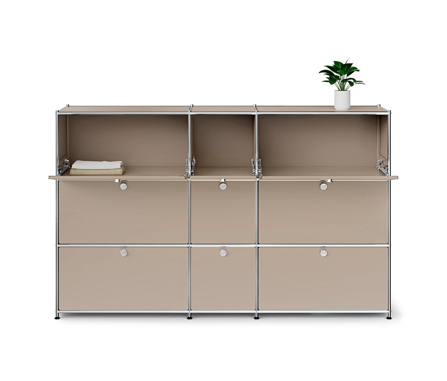 Beiges modulares Aufbewahrungsmöbel mit Chromrahmen, drei Reihen mit je drei Fächern. Die obere Reihe ist offen. Die mittlere Reihe hat zwei geschlossene und ein offenes Klappfach mit einem weißen Handtuch in einem Korb. Die untere Reihe hat drei geschlossene Klappfächer. Eine kleine grüne Pflanze in einem weißen Topf steht oben rechts.