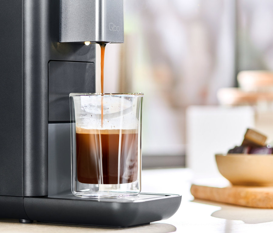 Kaffee läuft aus einer Qbo ESSENTIAL Dark Stone Kaffeemaschine in ein Glas.