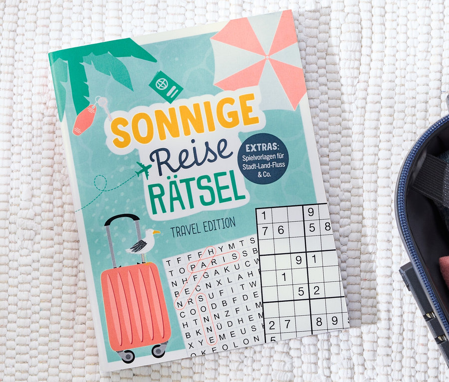 Buch »Sonnige Reise Rätsel« liegt neben einem offenen Koffer.
