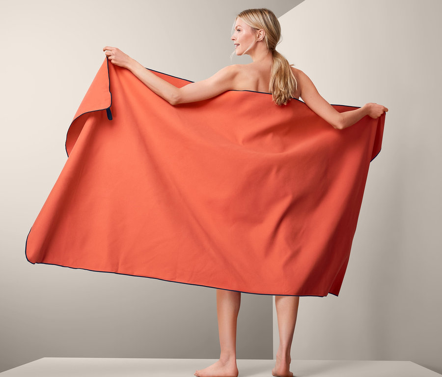 Frau hält XL-Outdoor-Badetuch, orange, ca. 100 x 200 cm.