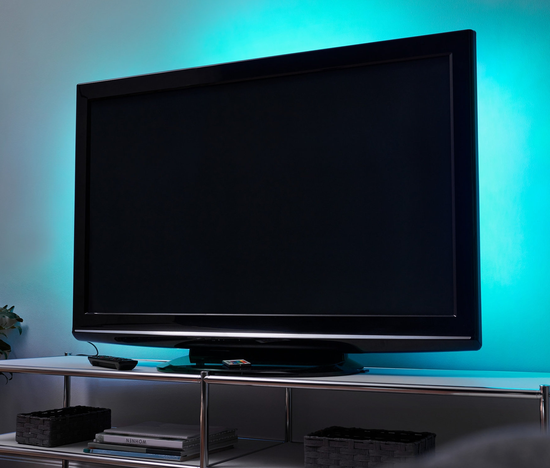 Fernseher mit LED-TV-Hintergrundbeleuchtung steht auf einem weißen Tisch. Im Hintergrund befindet sich eine Pflanze.