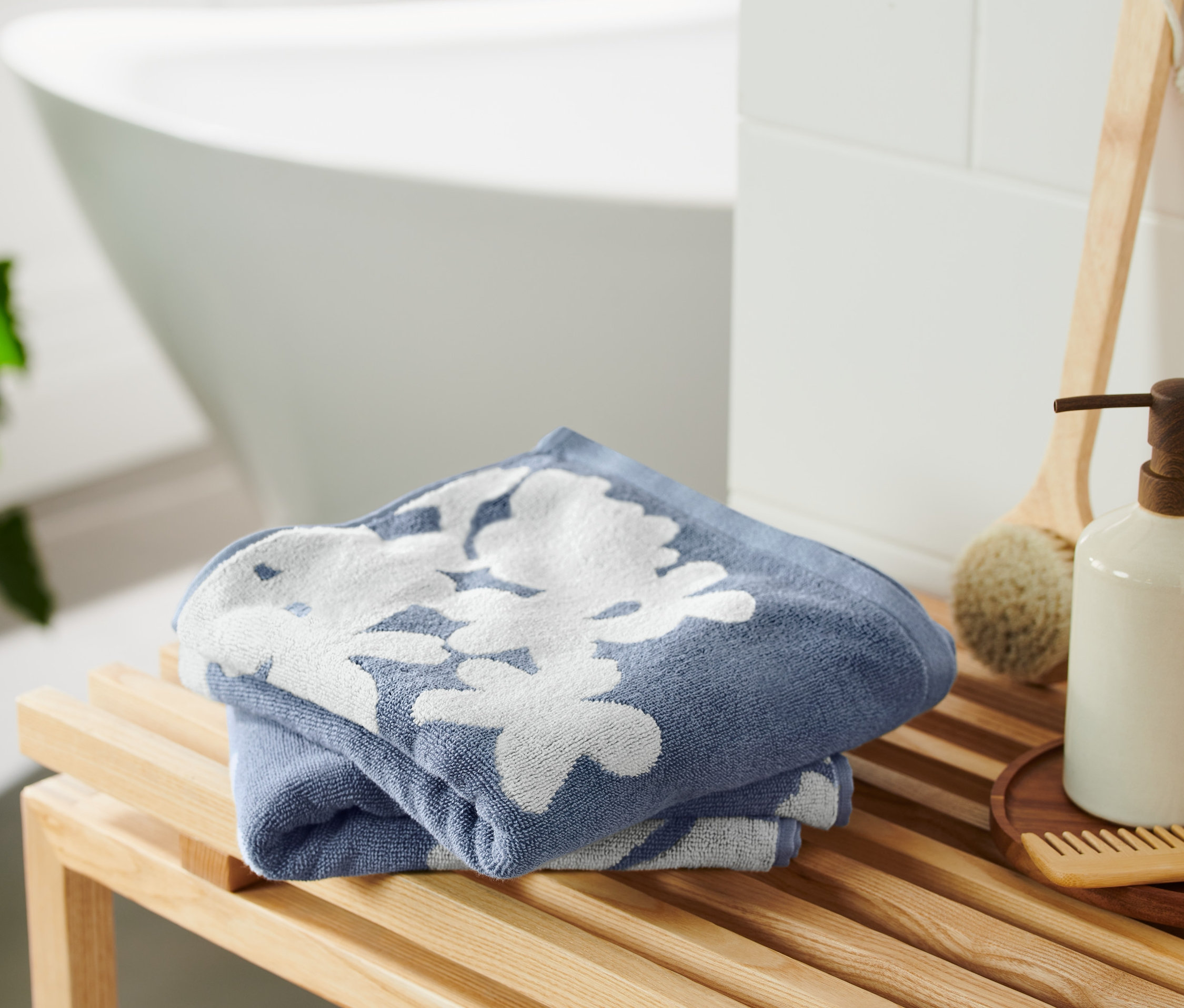 Zwei blaue Jacquard-Handtücher mit Blumenmuster liegen gefaltet auf einer Holzbank.