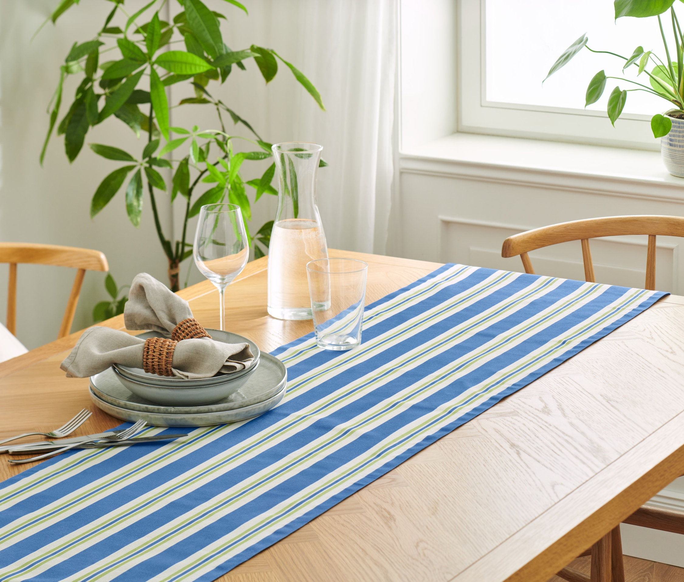 Gedeckter Tisch mit Baumwoll-Tischläufer, Streifen, Tellern, Gläsern und Leinentüchern.