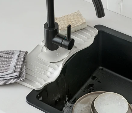 Eine Wasserhahn-Silikonablage befindet sich unter einem schwarzen Wasserhahn. Schmutziges Geschirr befindet sich im Spülbecken.