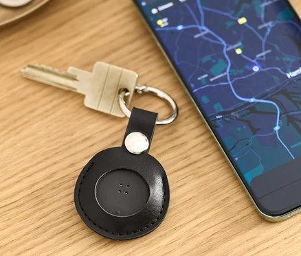 Auf einem Tisch liegen Schlüssel mit einem schwarzen Smart-Tracker mit Anhänger und ein Handy mit einer Karten-App.